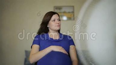 一个穿着蓝色连衣裙的孕妇正在享受风扇的气流。